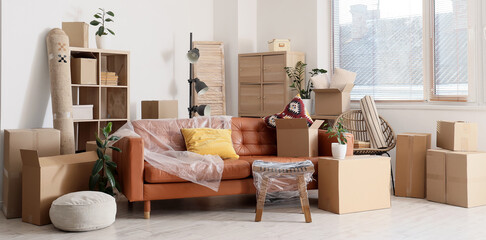 Brown sofa with film and cardboard boxes in living room on moving day