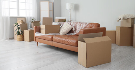 Brown sofa with film and cardboard boxes in living room on moving day