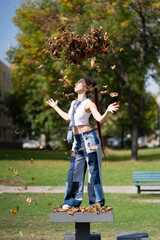 Vibrant woman with braids tossing utumn leaves in the air