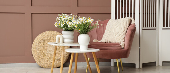 Interior of living room with armchair, tables and chamomiles in vases
