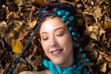 Woman with colorful braids finding peace lying among autumnal elements