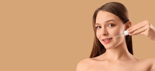 Pretty young woman with cosmetic serum on beige background with space for text