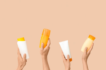 Female hands with bottles of sunscreen cream on beige background