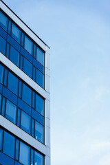 Photo shows the corner of a modern office building with blue glass windows and a clear sky...