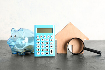 Calculator with piggy bank and wooden house on black table