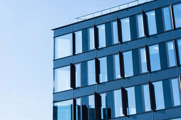 Contemporary office building facade with multiple open glass windows, reflecting clear blue sky....