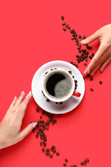 Female hands with cup of hot coffee and beans on red background