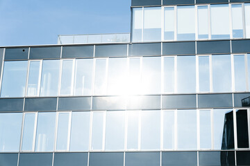 Contemporary office building exterior with large glass windows reflecting bright sunlight. Urban...
