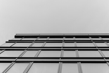 Black and white photo of a modern glass building facade viewed from below, emphasizing geometric...