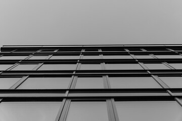 Black and white photo of a modern glass building facade viewed from below, emphasizing geometric...