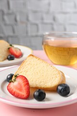 Piece of tasty bundt cake with berries and tea on pink table, closeup