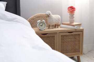 Bedside table with alarm clock, decor and books near bed indoors