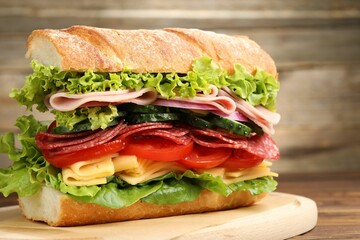 Tasty baguette sandwich with ham and vegetables on wooden table, closeup