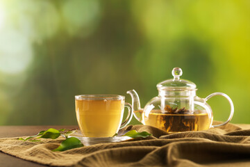 Cup of tasty green tea and teapot on table against blurred background