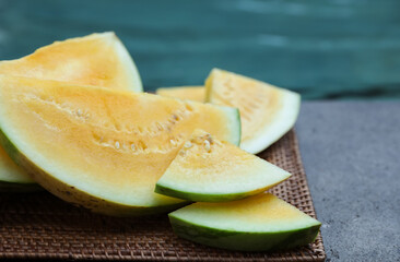 Pieces of ripe yellow watermelon on wicker table near swimming pool, closeup