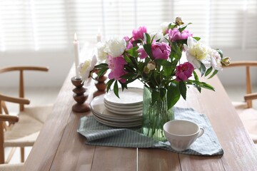 Dining table with beautiful flowers and dishware in room. Interior design