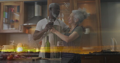 Clinking wine glasses couple wearing aprons at kitchen island with wine bottle and chopped veggies