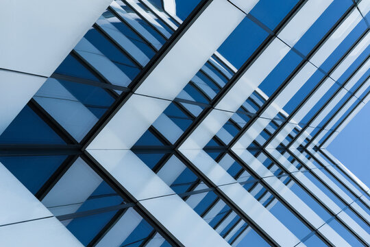 Abstract view of a modern glass building facade with strong geometric lines and blue sky reflections. Image emphasizes architecture, symmetry, and urban design.