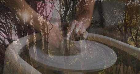 Shaping spinning clay with clay-coated hands on pottery wheel at studio, blending forest imagery