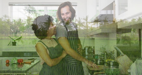 Embracing cooking couple stirring frying pan on stovetop at kitchen island, with tomatoes and herbs