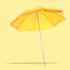 Bright beach umbrella casting shadow on pale yellow background