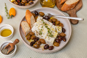 Feta cheese served on a plate with assorted olives, garnished with herbs and lemon slices and...