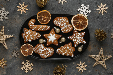 Plate of Christmas gingerbread cookies with dried orange slices and decorations on dark background