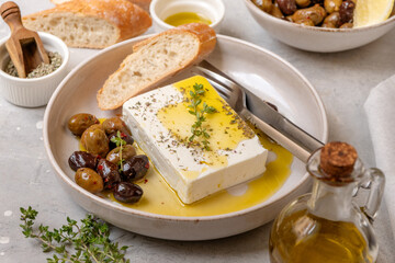 Feta cheese served on a plate with assorted olives, garnished with herbs and lemon slices and crusty bread, traditional Greek or Italian food, Mediterranean diet