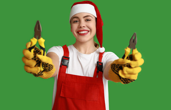 Young female construction worker in Santa hat with pliers on green background - Powered by Adobe