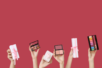 Female hands with eyeshadows palettes and gift boxes on dark red background