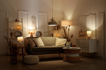 Comfortable sofa, chest of drawers, coffee table, pampas grass and glowing lamps in interior of...