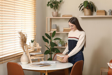 Young woman putting stack of books on table in living room
