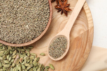 Wooden plate with different spices and spoon on light background
