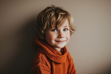 Cute little boy in warm orange sweater and scarf on grey background
