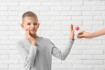 Little boy with tooth ache refusing from sweet lollipop on white brick background