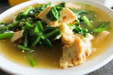 Close-up of Mie Tiktik, a dry noodle dish with chicken pieces and sauteed green vegetables, served on a white plate