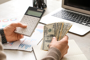 Male hands counting dollar banknotes while using calculator in office. Closeup