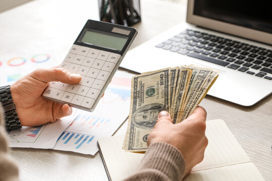 Male hands counting dollar banknotes while using calculator in office. Closeup