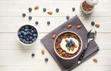 Bowl with chocolate tasty granola, yogurt, nuts and berries on white wooden background