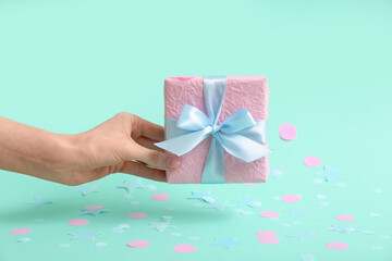 Female hand with gift box and pink confetti on turquoise background