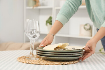 Young woman putting clean dishes on dining table at home, closeup