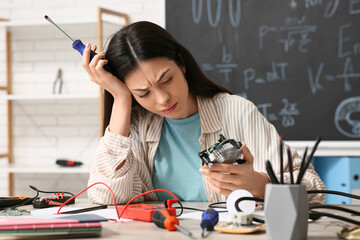 Upset female inventor with screwdriver and computer fan at table in workshop