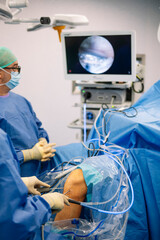 Surgeons inserting instruments during minimally invasive arthroscopic knee operation under camera...