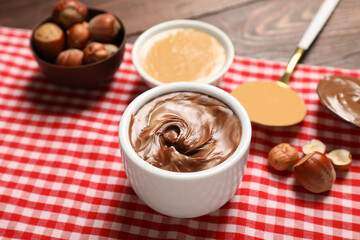 Bowls of sweet chocolate spread and nut butter on wooden background, closeup