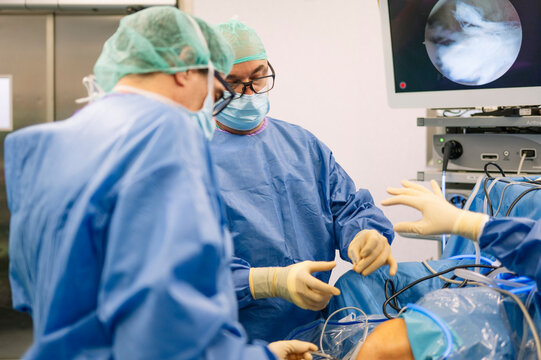 Focused surgeons performing arthroscopic procedure on patient’s knee using specialized surgical instruments
