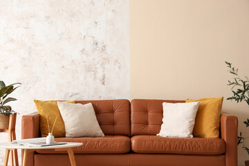 Interior of living room with brown leather sofa, houseplants and coffee table near grunge wall
