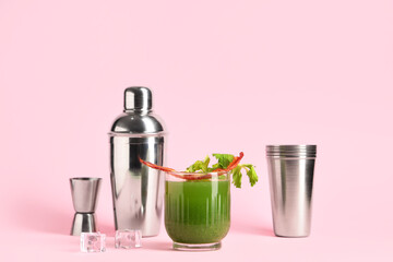Glass of green bloody mary cocktail with bacon, celery and ice cubes on pink background