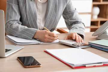 Calculator and female accountant writing in notebook at table