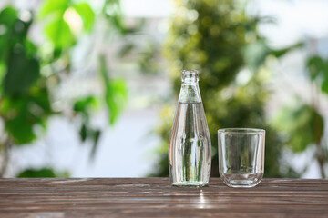 Bottle of water and glass on wooden table outdoors