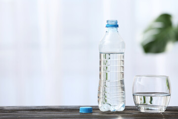 Bottle of water and glass on wooden table indoors
